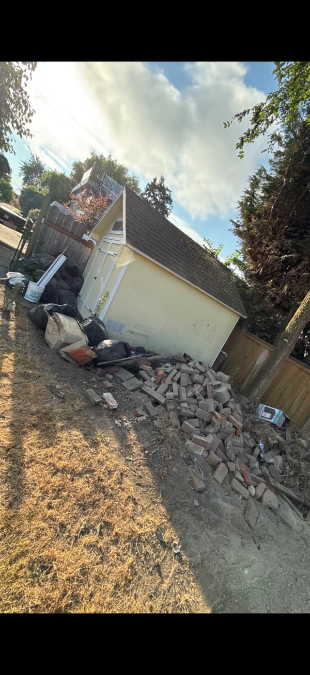 Yard debris and masonry stacked beside an outbuilding before removal